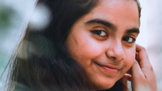 Young woman looking over her shoulder smiling, with out of focus leaves in the foreground